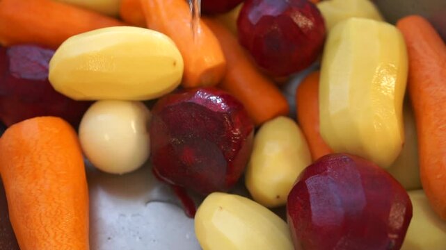 Vegetables in the sink under a stream of water from a tap. Preparation Ukrainian borscht, peeled carrots, beets, and potatoes are seen being washed in a sink.