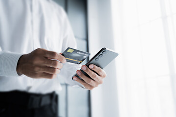 Asian male hold credit card and use mobile phone for online transactions.