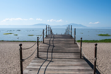 Rustic wooden pier stretches over sandy beach into peaceful Lake Chapala, Jalisco, Mexico