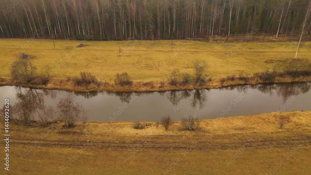 Poster Aerial view of a winding river through autumn fields and forests under an overcast sky, with visible power lines crossing the open land.