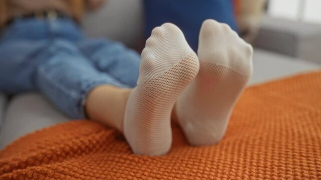 Woman relaxing on sofa with feet in white socks on orange blanket in cozy living room.