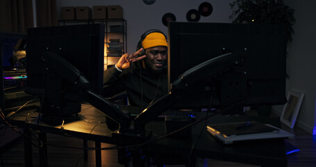 Wearing a hoodie and cap, a man works on music in a dark room filled with LED light. He waves his hands to the rhythm, feeling the vibe of the rap he is producing.