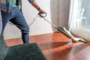 Fototapeta premium Cleaning hardwood floor with vacuum cleaner, bright sunlight illuminating modern apartment interior