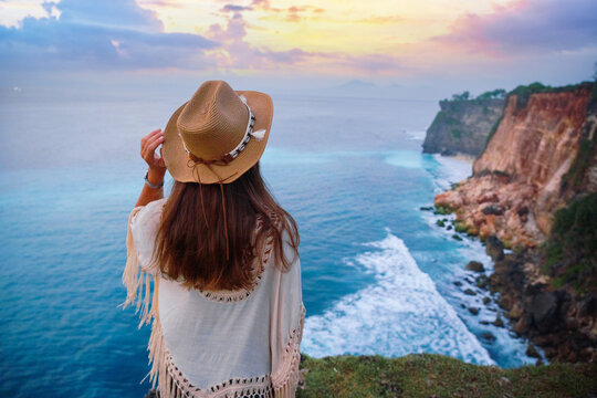 Calm free alone traveler girl wearing hat enjoys turquoise stunning ocean view on cliff during traveling at beautiful destination on Bali island, Indonesia