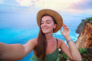 Selfie portrait photo of a joyful smiling traveler woman with closed eyes wearing hat enjoys...