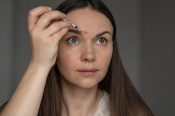 Fototapeta premium Young woman giving beauty injection to her face while looking in the mirror. Close-up. Home skin care and aesthetic procedures