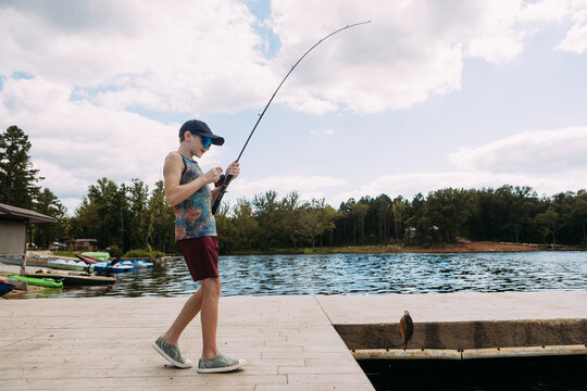 Preteen on dock reeling fish on fishing rod from lake