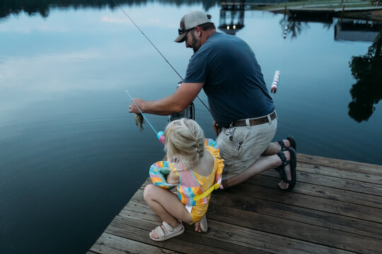 Dad helping young daughter while fishing on summer evening