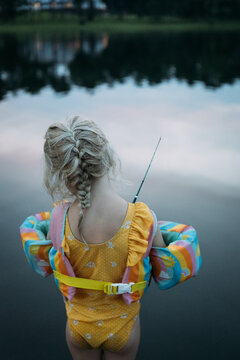 Little girl fishing on lakeside during summer evening