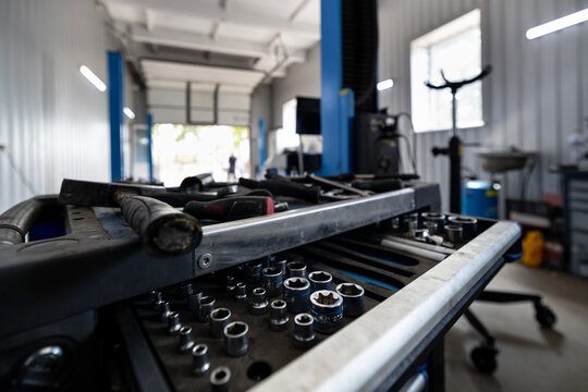 A rolling tool cart filled with sockets and various hand tools sits in a spacious auto repair shop with lifts and other equipment.
