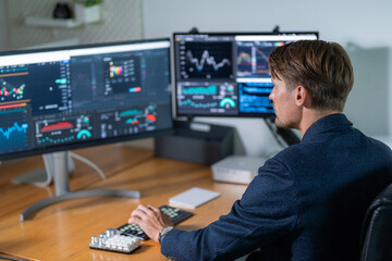 Professional trader analyzing market trends at a modern workstation with multiple monitors in a...