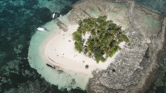 Breathtaking drone view of a tropical island in the Philippines, surrounded by crystal-clear waters and coral reefs. A white sand beach meets lush palm trees, with boats and tourists enjoying paradise
