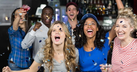 Image of confetti falling over happy diverse group of friends drinking in bar