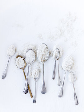 Overhead view of a Row of assorted silver spoons filled with flour on a white background