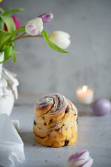 Easter Bread or Kulich with raisins. Easter yeast twisted cake Cruffin, painted eggs and tulip flowers on a stone background. Easter food.
