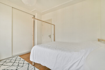 A serene and clean minimalist bedroom showcasing a white bed, wooden fixtures, and bright natural light. The design emphasizes simplicity and tranquility.