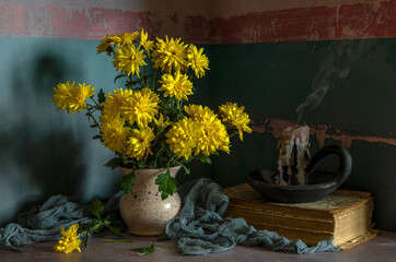 A bouquet of yellow chrysanthemums and an extinguished candle, on a dark background.