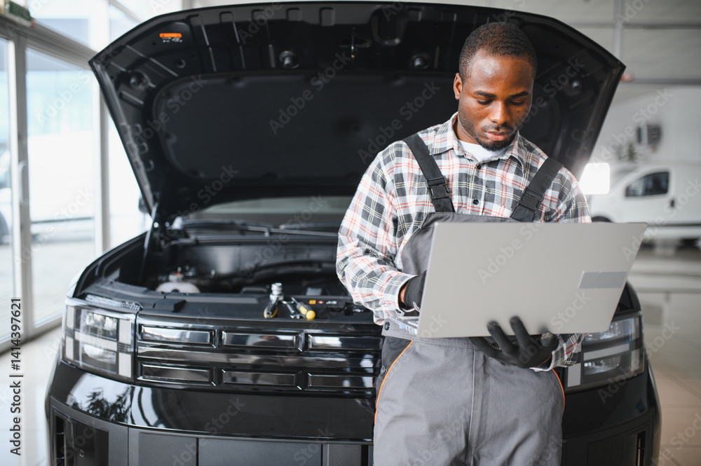 Poster Black auto mechanic running diagnostic on laptop while analyzing engine problems in a workshop