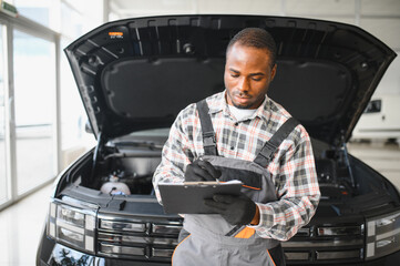 Mechanic carefully inspecting car in auto repair shop with clipboard. Focused professional...