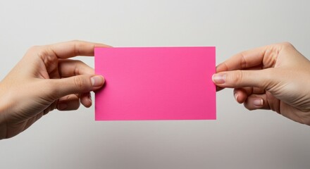 Obraz premium Two hands holding a bright pink rectangular card against a plain neutral background in horizontal view