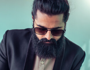 Obraz premium Portrait of a fashionable man with a thick beard and sunglasses, dressed in a formal suit, exuding confidence and style while wearing a contemporary expression against a relaxed, modern background.