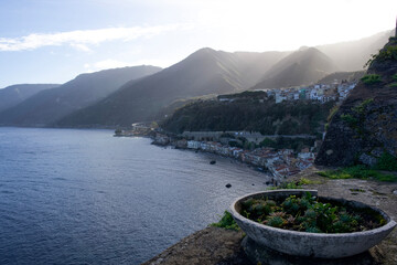 A wide view from a coastal ledge features mountains rising behind a hillside of Scilla in Italy...