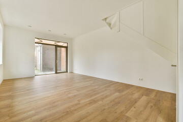 A bright and spacious interior showcases a minimalist design, featuring wooden floors and large windows providing ample natural light.