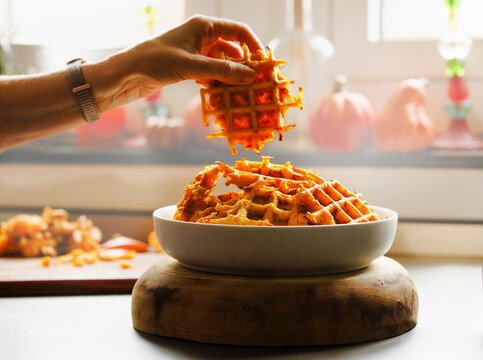 Women hand holding delicious pumpkin waffles on kitchen table with autumn decoration