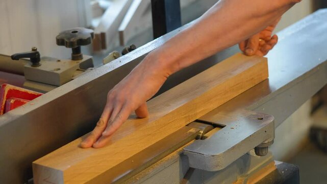 Skilled woodworker using electric jointer, hands guiding timber removing rough edges. Smoothness, flawless finish, expert handling and shaping, high quality craftsmanship, workpiece roughness turning