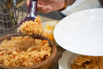 A person serving a portion of delicious fried rice from a wooden bowl onto a plate. The scene captures a culinary moment at a dining table, showcasing freshly prepared food and appetizing details.