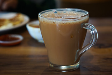 A close-up of tea served in glasses on a wooden table, paired with flatbreads and sauces, depicting a cozy breakfast or snack setting in natural light