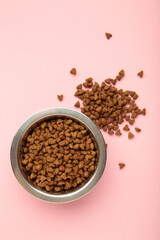 Dog or cat dry food in a silver bowl on pink background. Vertical photo