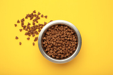 Dog or cat dry food in a silver bowl on yellow background