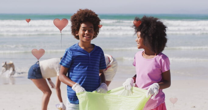 Image of hearts over african american female and male volunteers picking up rubbish on beach