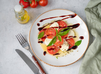 Fresh Caprese salad with sliced ​​tomatoes, mozzarella cheese, basil leaves and balsamic glaze