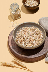 Oat flakes in bowl with wheat and napkin on a wooden board on a yellow background.