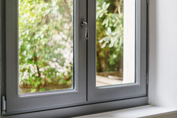 Fototapeta premium Modern window frame in a living room overlooking a lush green garden
