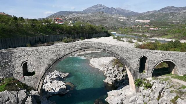 Old stone bridge over the river. Water flows under the bridge. Mesi Bridge on the Kir River, Shkoder, Albania, built in the 18th century. Ottoman architecture. Tourist attraction.