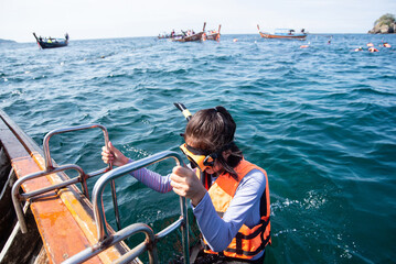 Women wearing a life jacket with snorkeling equipment holding boat ladder prepare snorkeling...