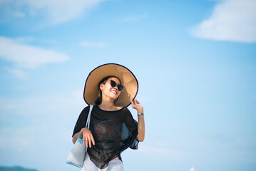 An Asian woman feeling relaxed and happy wearing sunglasses, hat, See-through hand holding a hat on...