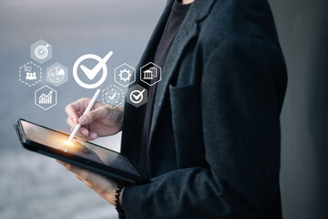 A person holds a tablet while using a stylus, with floating icons around them including a checkmark, chart, gear, and globe—symbolizing digital approval, analysis, and global access.