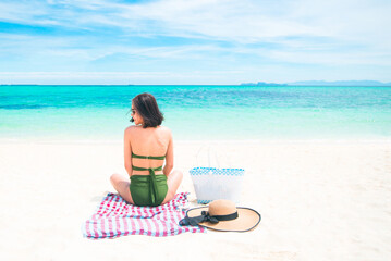 Long shot Asian Women tan skin being sunbathed comfort posture sitting on the cotton at the beach with the seaside background. Comfortable holiday vacations and relaxing travel concept. Copy space.