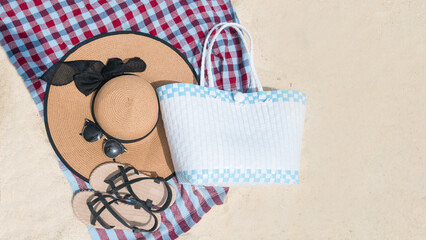 Top view Slippers, Straw Hat, and a bag on the cotton or accessories of the sea travel on a sandy beach. holiday summer relaxing and travel concept. The emotion of comfortable. Copy space for text.