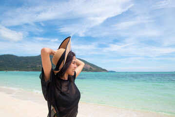 Asian woman wearing sunglasses, hat, See-through, and bikini. hand holding a hat on the beach with clear sea and sky background. long weekend holidays and travel concept. Relaxed. Copy space for text.