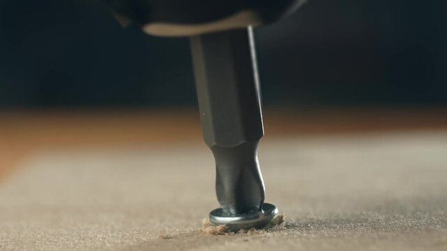 Close-up screwdriver bit screwing countersunk self-tapping screw into wooden surface. Hardware tool gradually driving pointed fastener during repair. Metal bit working with screw in construction scene