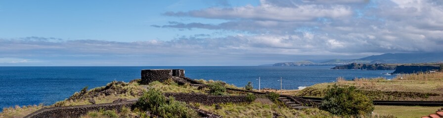 Fototapeta premium Friedliche Aussicht am Miradouro da Tromba de Elefante. Runde Umrandung aus Lavasteinen im Vordergrund, Blick auf die grüne Nordküste bis Fenais da Luz, das blaue Meer strahlt Ruhe aus.