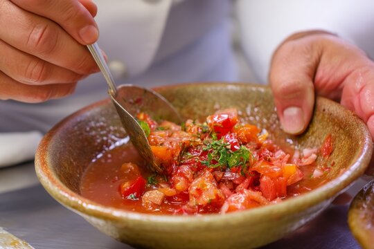 Chirmol in bowl with rustic texture, hands holding spoon above salsa made of tomatoes, onions, herbs. Concept of Chirmol highlights warmth of Guatemalan chile sauce stew.