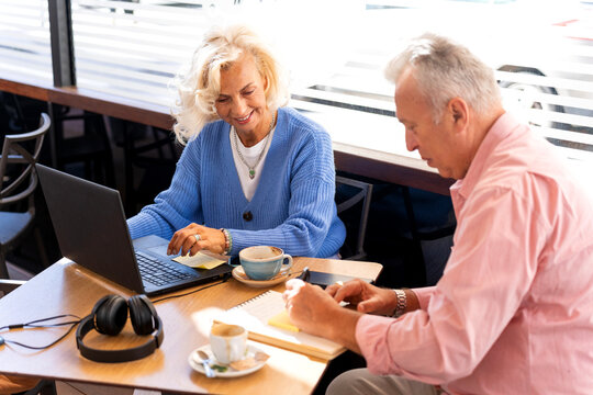 Senior russian couple working on laptop and taking notes in cafe - Powered by Adobe
