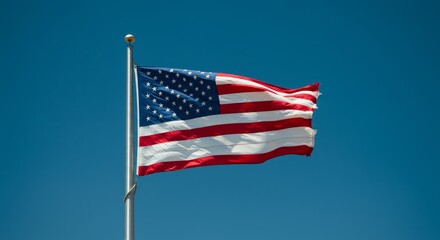 Fototapeta premium American Flag Waving in Blue Sky - A vibrant American flag billows proudly against a clear, bright blue sky. Patriotic symbol of freedom