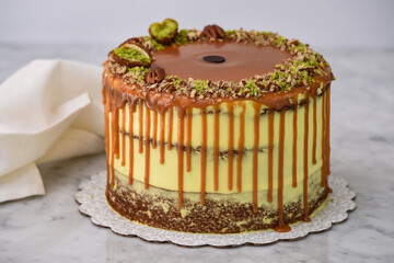 Pistachio Caramel Drip Cake featuring layers of moist cake drizzled with rich caramel, topped with chopped pistachios, and pecan halves with napkin on grey background side view of baked dessert